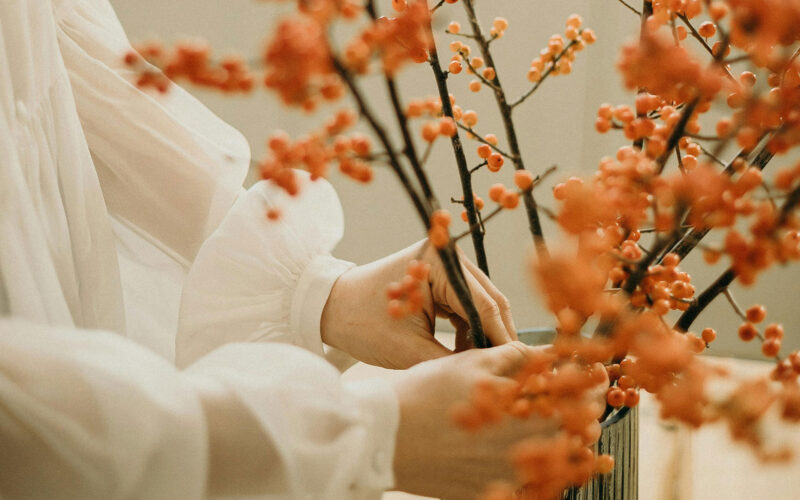 Close up of woman putting fall flowers in a vase